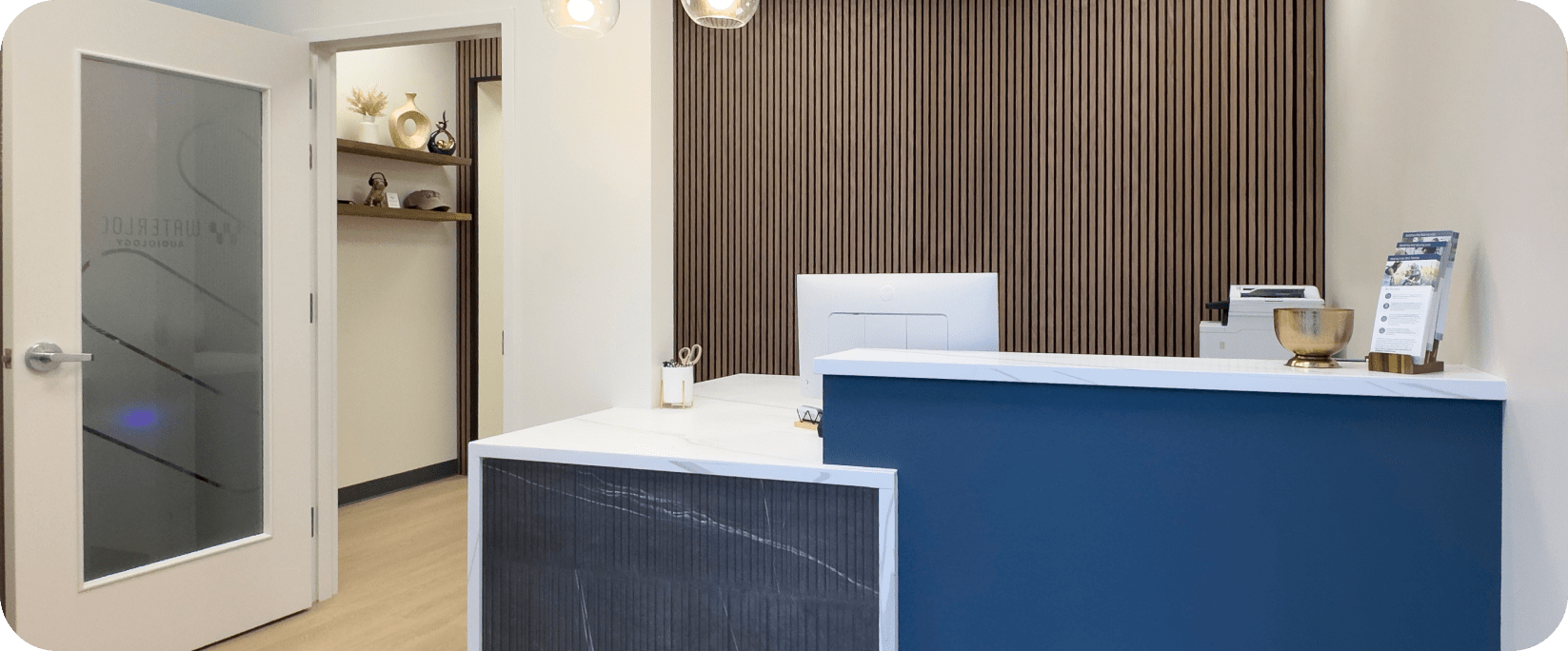 http://Modern%20audiology%20office%20reception%20area%20with%20blue%20and%20white%20desk,%20and%20a%20frosted%20glass%20door.